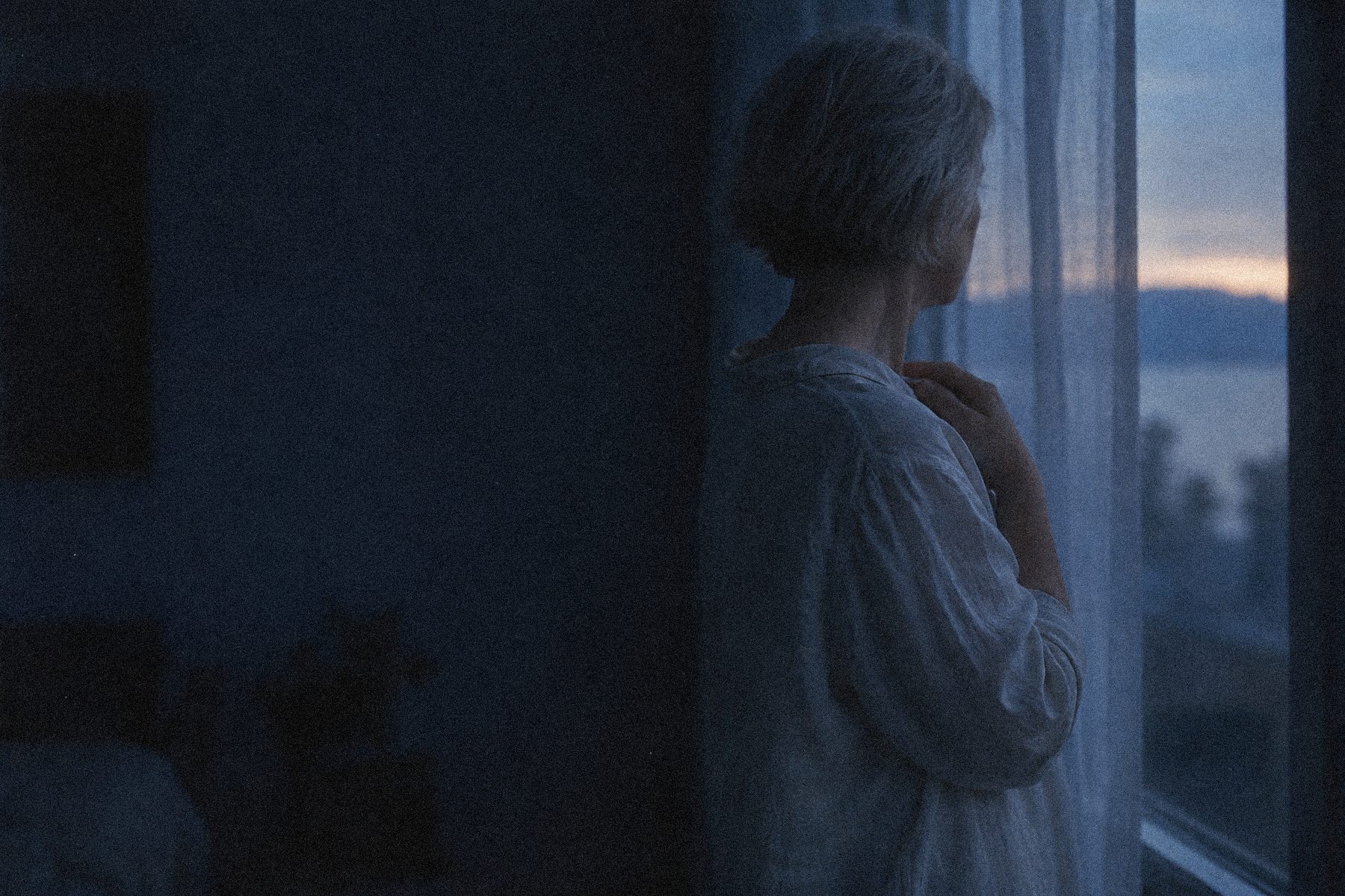 Woman with silver hair by a window at dusk
